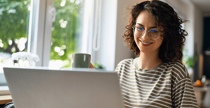 A woman wearing glasses is smiling while looking at a screen